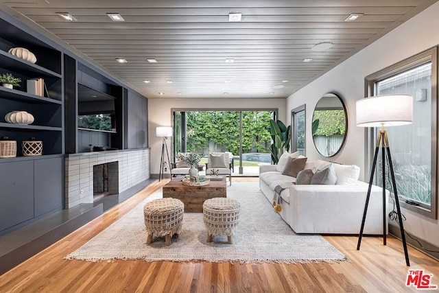 living room featuring built in shelves, a fireplace, wooden ceiling, and light wood-type flooring