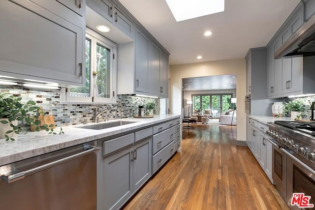 kitchen with stainless steel appliances, sink, gray cabinetry, and a skylight