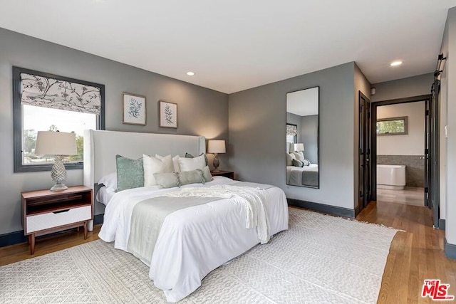 bedroom with hardwood / wood-style floors, a barn door, and ensuite bathroom