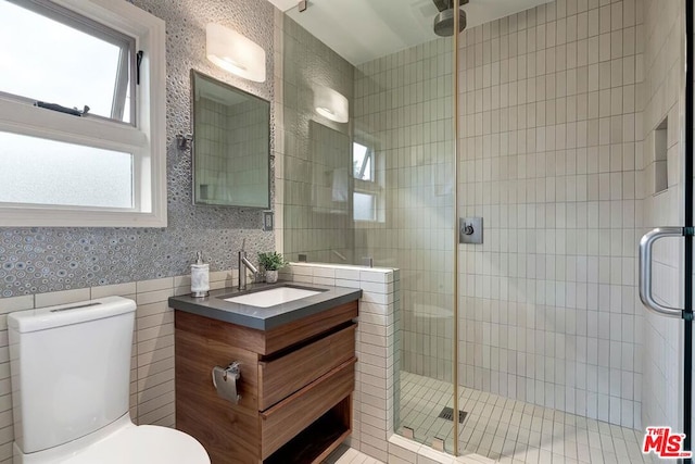 bathroom featuring vanity, a shower with door, tile walls, and toilet