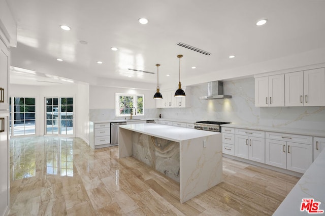 kitchen featuring white cabinetry, decorative light fixtures, a center island, stainless steel dishwasher, and wall chimney range hood