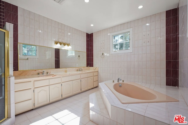 bathroom featuring tiled tub, vanity, tile patterned flooring, and tile walls