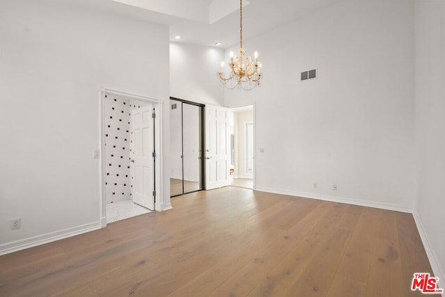 empty room with hardwood / wood-style flooring, a chandelier, and a towering ceiling