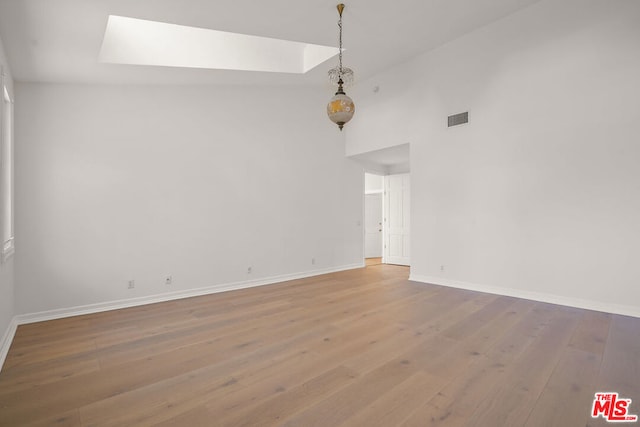 unfurnished room featuring a skylight, light hardwood / wood-style floors, and a high ceiling