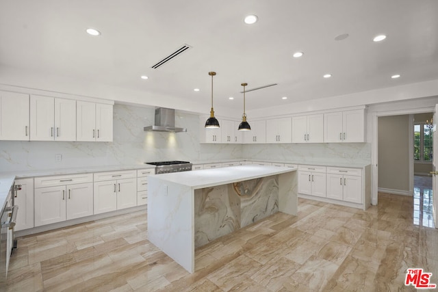 kitchen featuring a kitchen island, white cabinetry, hanging light fixtures, light stone counters, and wall chimney exhaust hood