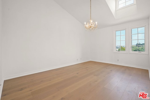 empty room featuring a notable chandelier, vaulted ceiling, and light wood-type flooring