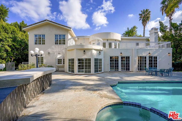 back of property with a balcony, a pool with hot tub, and a patio