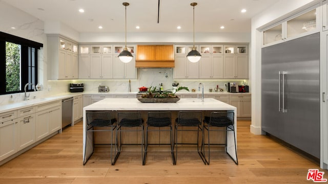 kitchen featuring stainless steel appliances, light hardwood / wood-style floors, hanging light fixtures, and a center island with sink