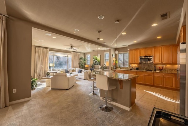 kitchen featuring appliances with stainless steel finishes, a breakfast bar, decorative light fixtures, sink, and light stone countertops