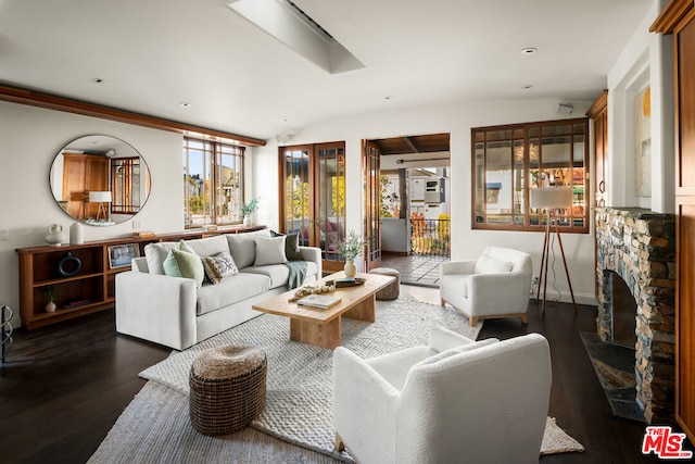 living room with a stone fireplace, dark wood-type flooring, and vaulted ceiling with skylight