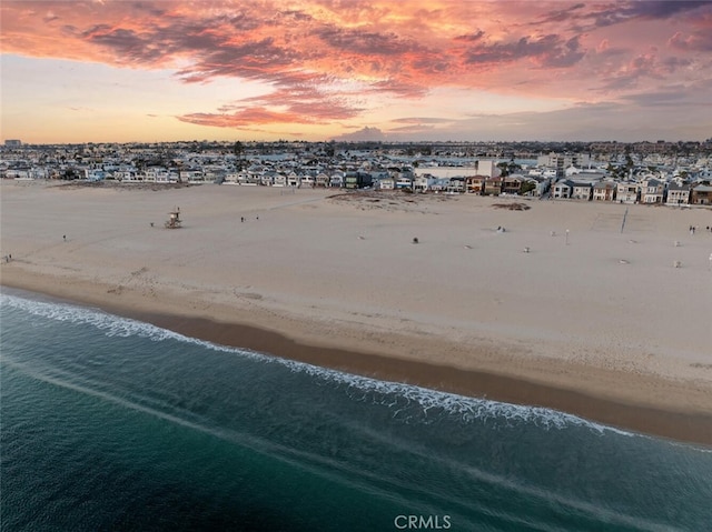 aerial view at dusk featuring a water view and a view of the beach