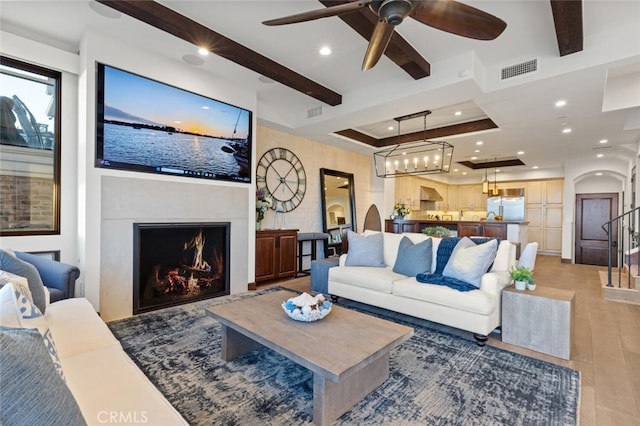 living room featuring beamed ceiling, a raised ceiling, ceiling fan, and light hardwood / wood-style floors