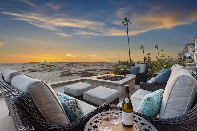 patio terrace at dusk featuring a view of the beach, a water view, and an outdoor fire pit