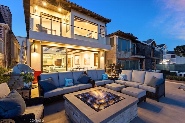 patio terrace at dusk featuring a balcony and an outdoor living space with a fire pit