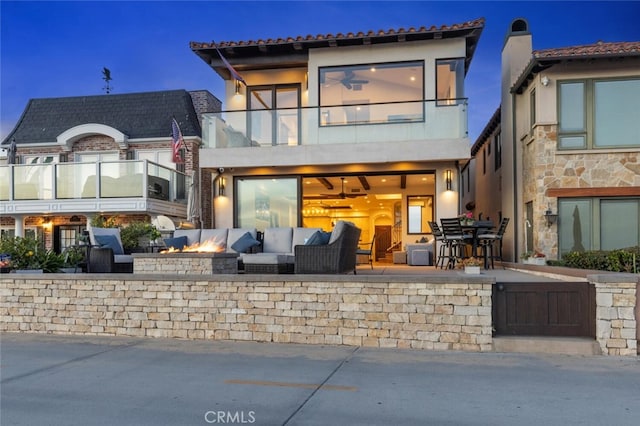 back of house with a balcony, a patio area, and an outdoor living space with a fire pit