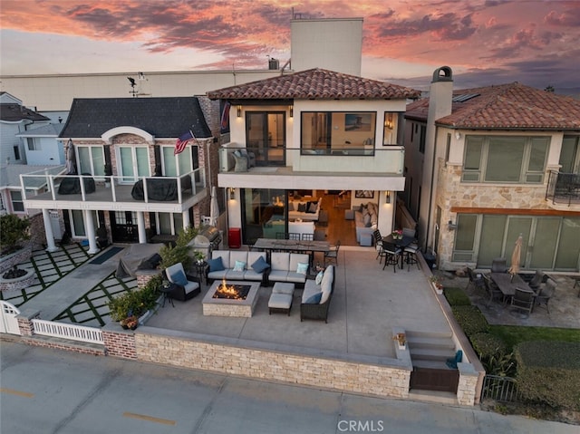 back house at dusk featuring a balcony, a patio, and an outdoor living space with a fire pit