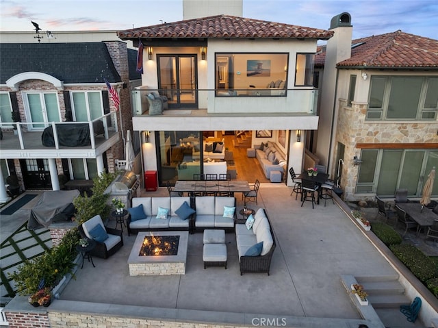 back house at dusk featuring a patio area and an outdoor living space with a fire pit