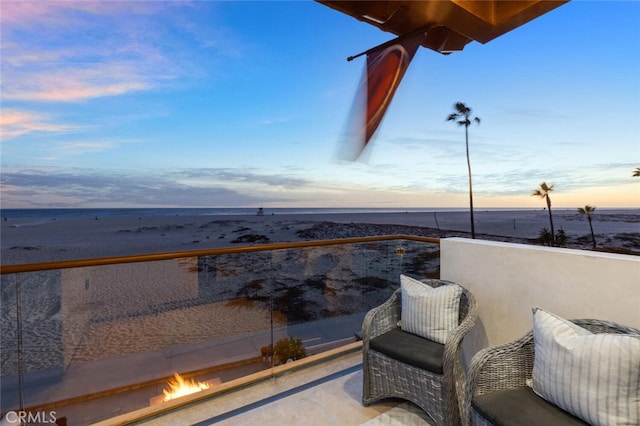 balcony at dusk featuring a water view and a view of the beach