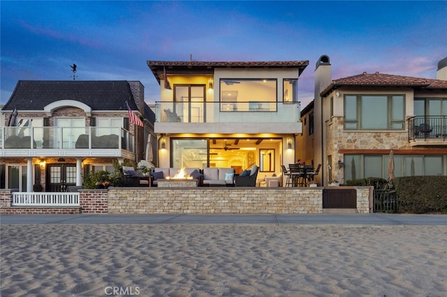 back house at dusk featuring a balcony, an outdoor fire pit, and a patio