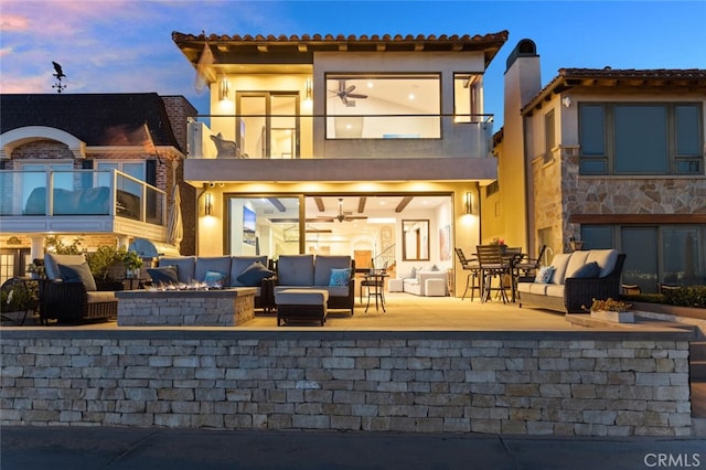 back house at dusk with a patio, a balcony, and an outdoor hangout area