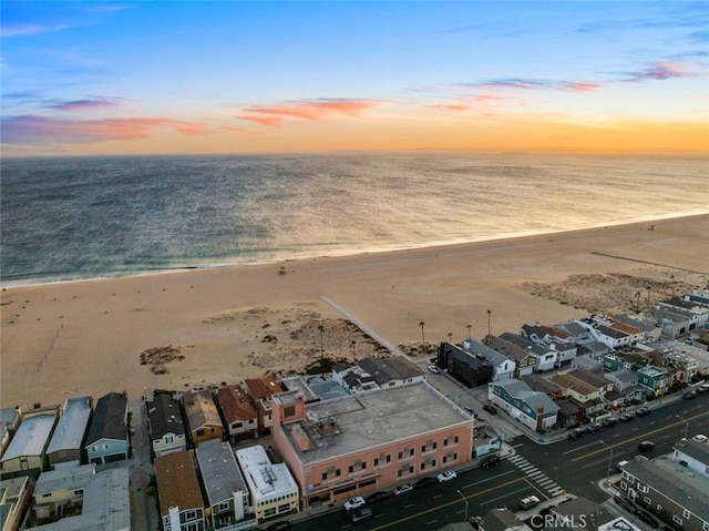 aerial view at dusk with a water view and a view of the beach