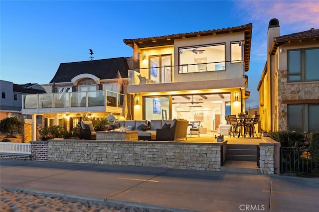 back house at dusk featuring an outdoor living space, a patio, and a balcony