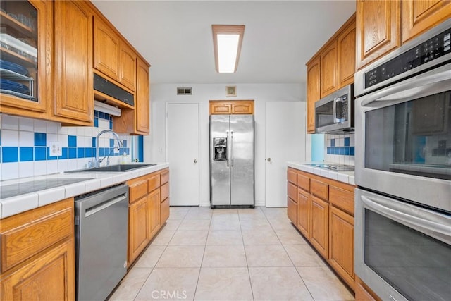 kitchen featuring tasteful backsplash, sink, tile counters, light tile patterned floors, and stainless steel appliances