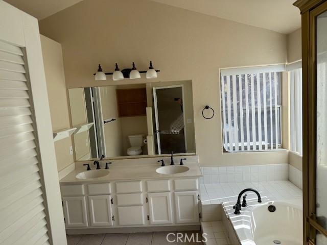 bathroom featuring lofted ceiling, vanity, a relaxing tiled tub, tile patterned floors, and toilet