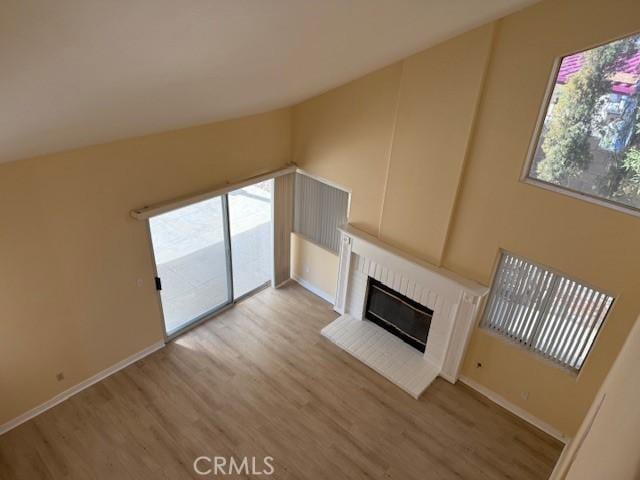 unfurnished living room featuring a healthy amount of sunlight, light hardwood / wood-style floors, and a brick fireplace