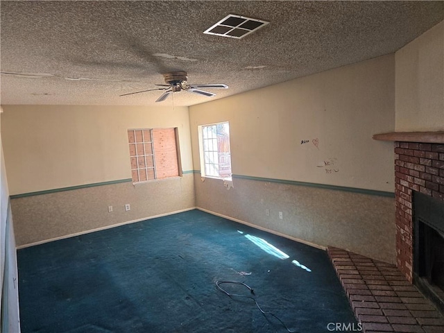 carpeted spare room featuring a brick fireplace, a textured ceiling, and ceiling fan