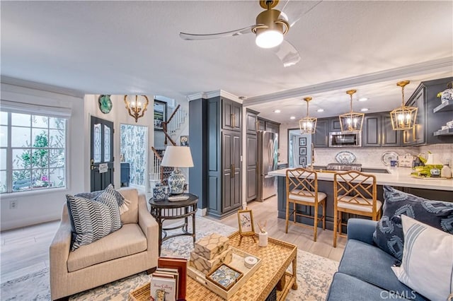 living room with ceiling fan with notable chandelier, ornamental molding, and light hardwood / wood-style floors