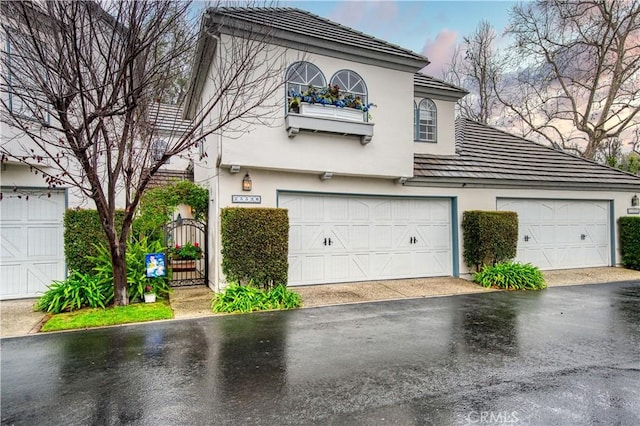 view of front facade with a gate, a garage, driveway, and stucco siding