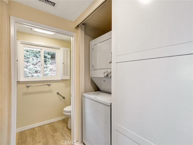 interior space featuring stacked washer / drying machine, hardwood / wood-style floors, and toilet