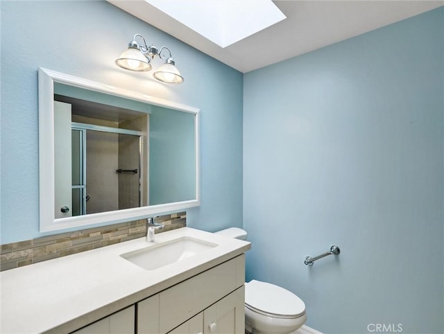 bathroom with a shower with door, a skylight, tasteful backsplash, vanity, and toilet