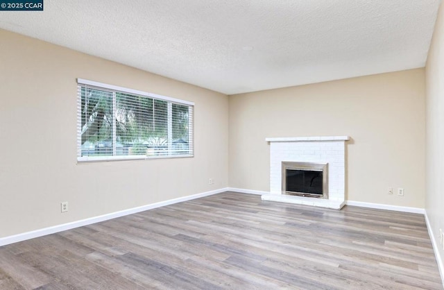 unfurnished living room featuring a brick fireplace, light hardwood / wood-style floors, and a textured ceiling