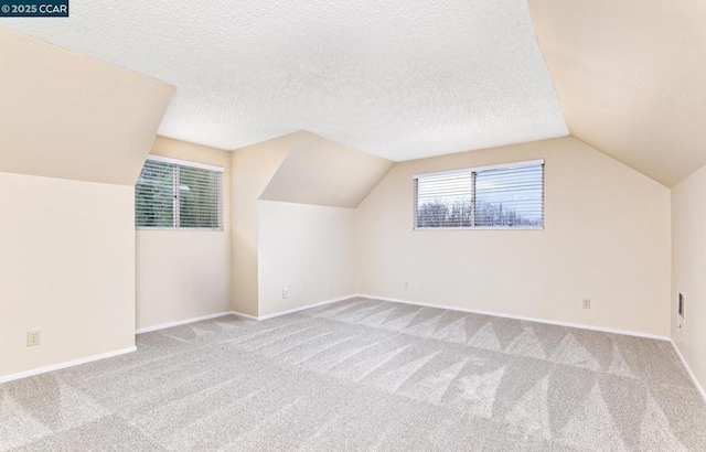 additional living space featuring light colored carpet, vaulted ceiling, and a textured ceiling