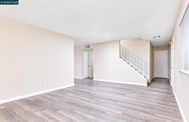 unfurnished living room featuring a textured ceiling and light hardwood / wood-style floors