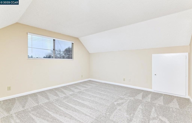 additional living space with vaulted ceiling, light colored carpet, and a textured ceiling