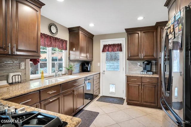 kitchen with sink, light tile patterned floors, black refrigerator, light stone countertops, and stainless steel dishwasher