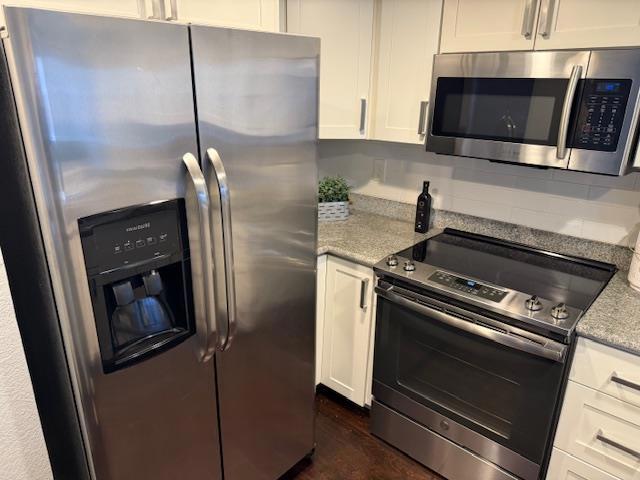 kitchen featuring stainless steel appliances, white cabinetry, light stone countertops, and backsplash