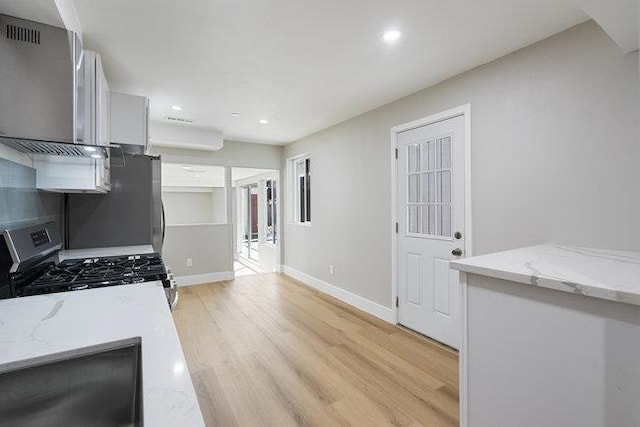 kitchen featuring light stone counters, gas range, light hardwood / wood-style floors, and white cabinets