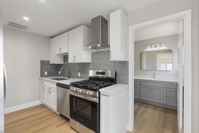 kitchen featuring appliances with stainless steel finishes, sink, wall chimney range hood, and white cabinets