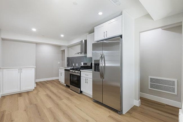 kitchen with stainless steel appliances, wall chimney range hood, white cabinets, and light hardwood / wood-style floors