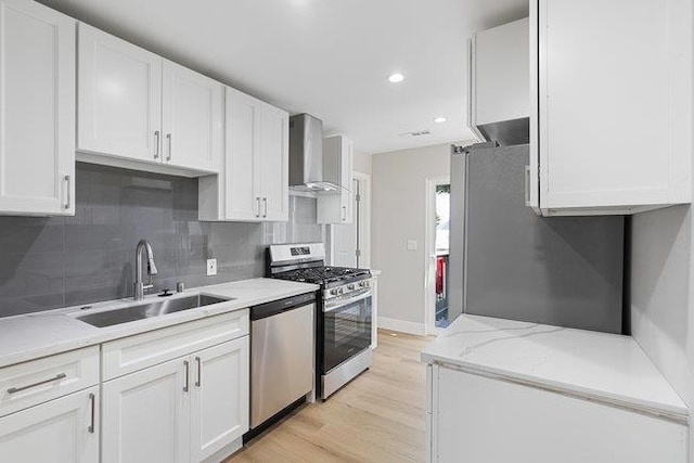 kitchen featuring wall chimney exhaust hood, sink, light hardwood / wood-style flooring, stainless steel appliances, and white cabinets