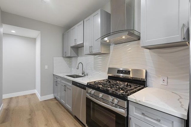 kitchen with wall chimney exhaust hood, sink, light stone counters, tasteful backsplash, and stainless steel appliances