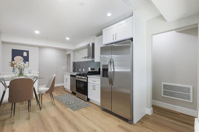 kitchen with tasteful backsplash, white cabinets, stainless steel appliances, wall chimney range hood, and light wood-type flooring