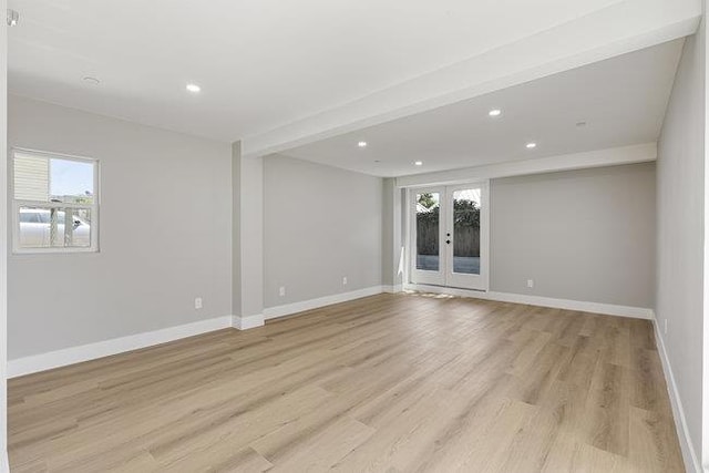 empty room with french doors, plenty of natural light, beam ceiling, and light hardwood / wood-style flooring