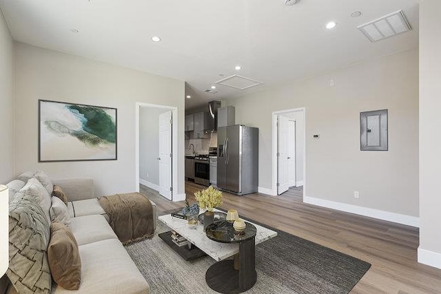 living room with sink, electric panel, and light wood-type flooring