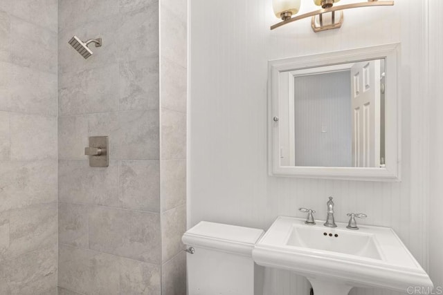 bathroom with a tile shower, sink, and toilet