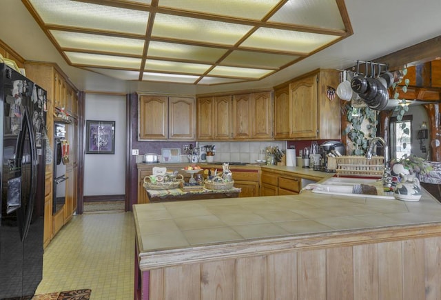 kitchen featuring sink, decorative backsplash, tile counters, black fridge with ice dispenser, and kitchen peninsula